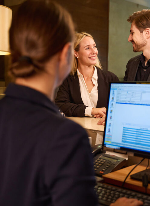 Woman receptionist checking in happy guy and lady who standing near reception desk and looking at each other